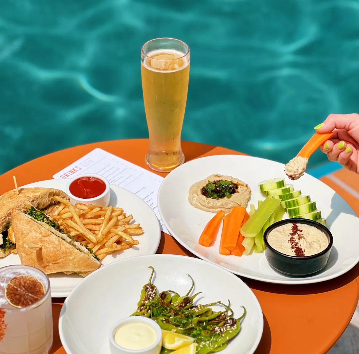A selection of meals and a beer on a table beside a pool