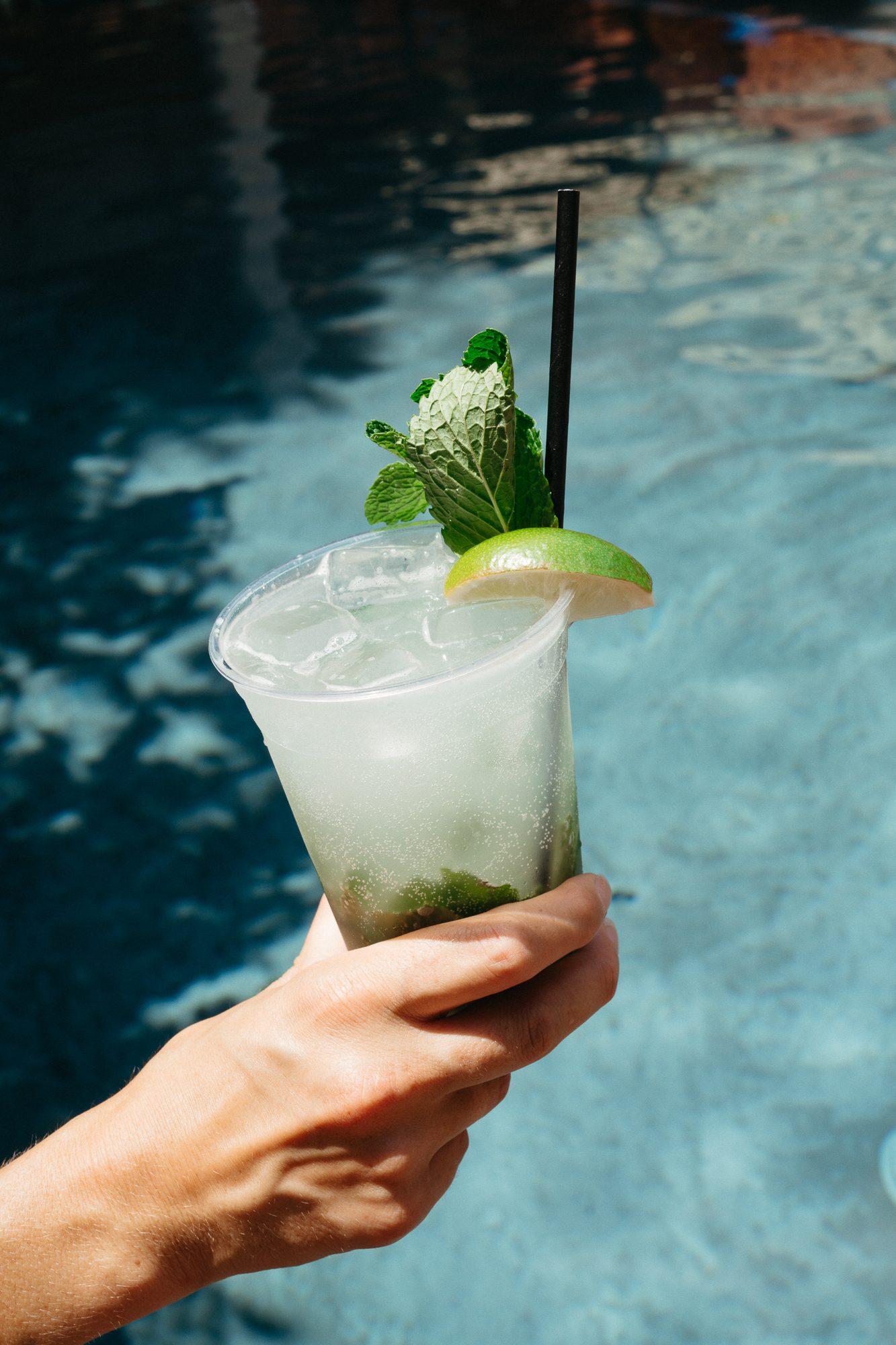 A hand holding a cocktail by the Carpenter Hotel pool