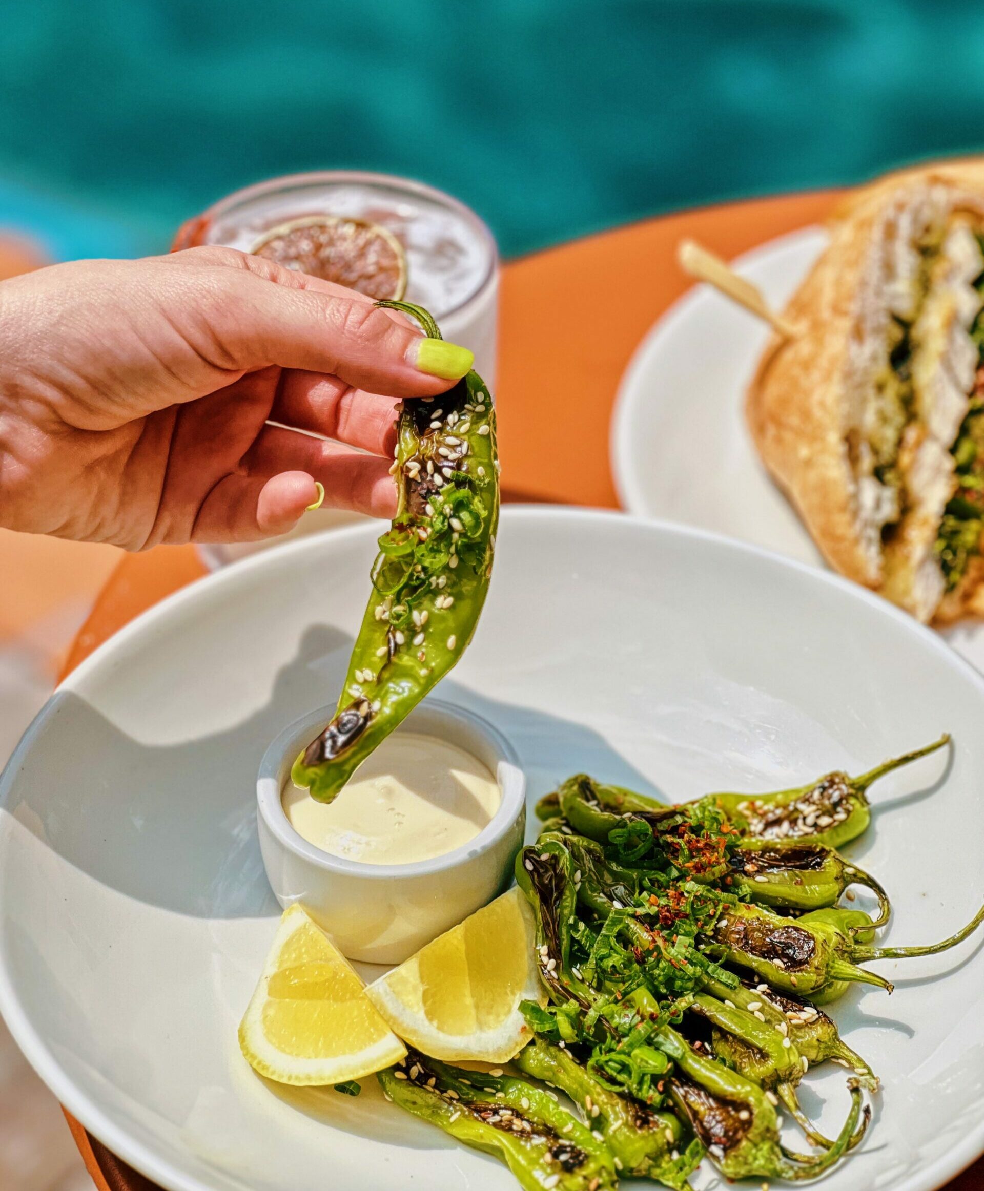A hand dipping a roasted chilli into a dipping sauce