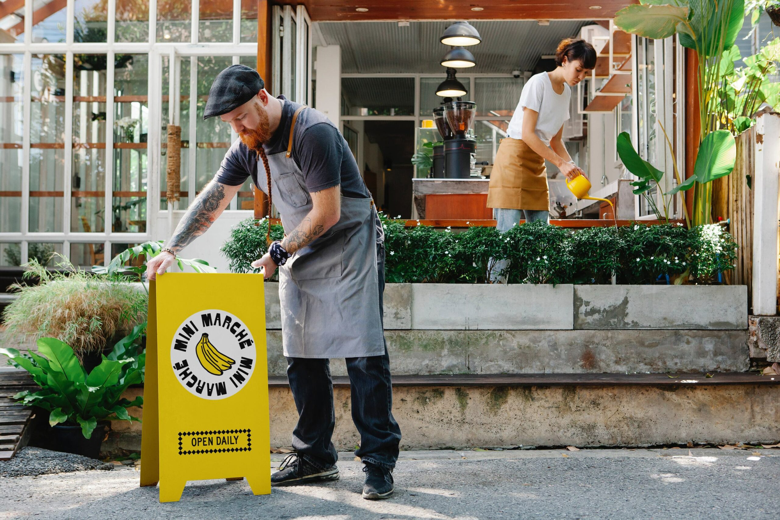two people outside man setting up a yellow sign and woman watering plants