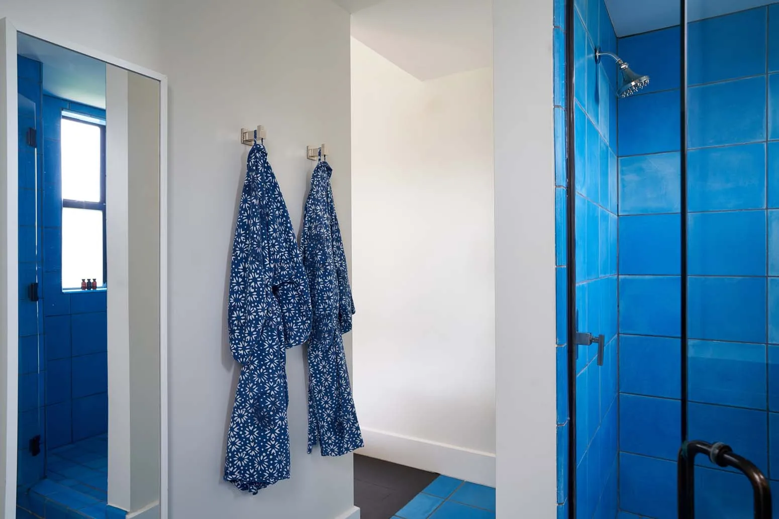 Blue robes hanging in the bathroom with a blue tiled shower in the Studio Suite