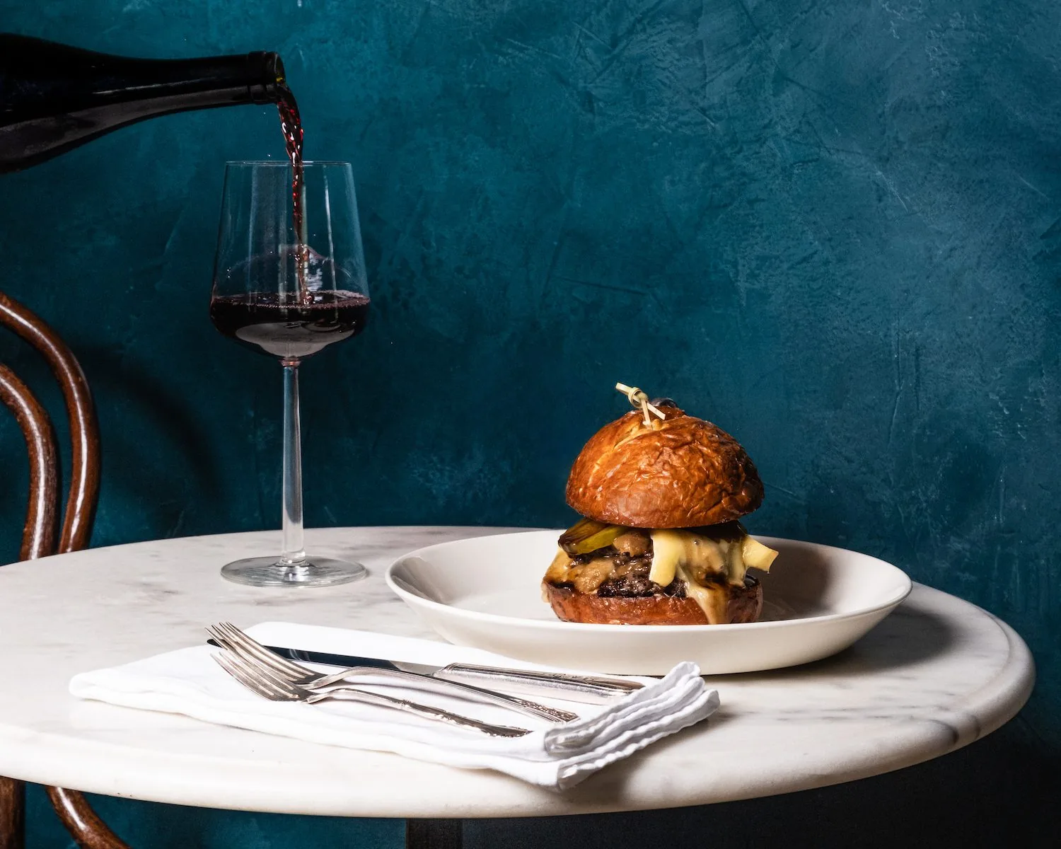 burger on a table with a glass of wine being poured