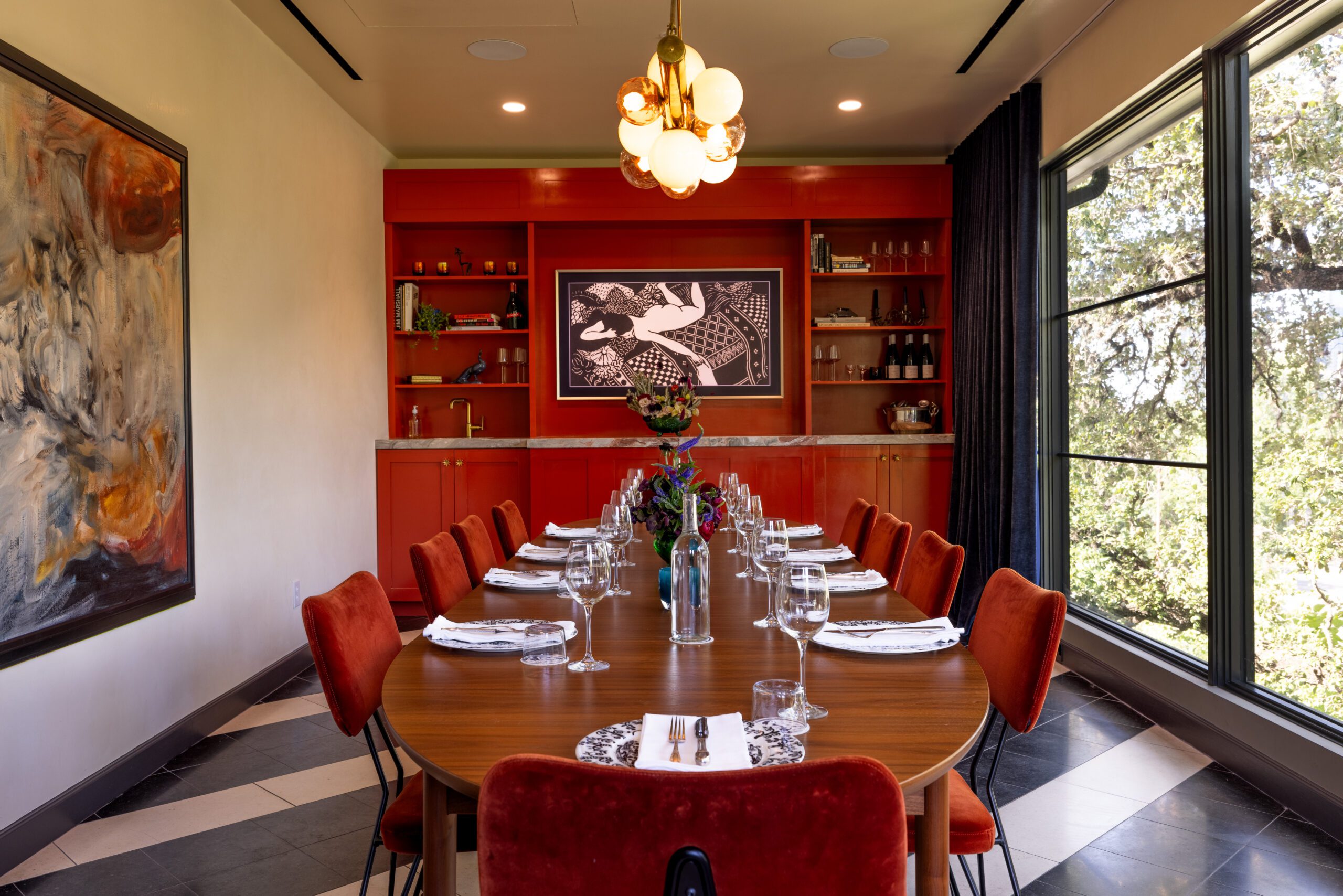 A long dinner table in a room with red cabinetry, with place settings