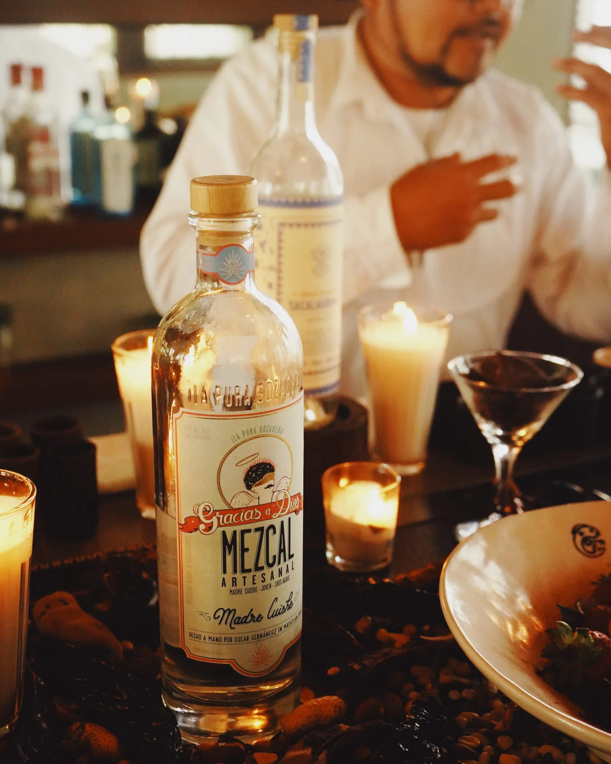 Bottles of mezcal, glasses, food and candles on a dinner table