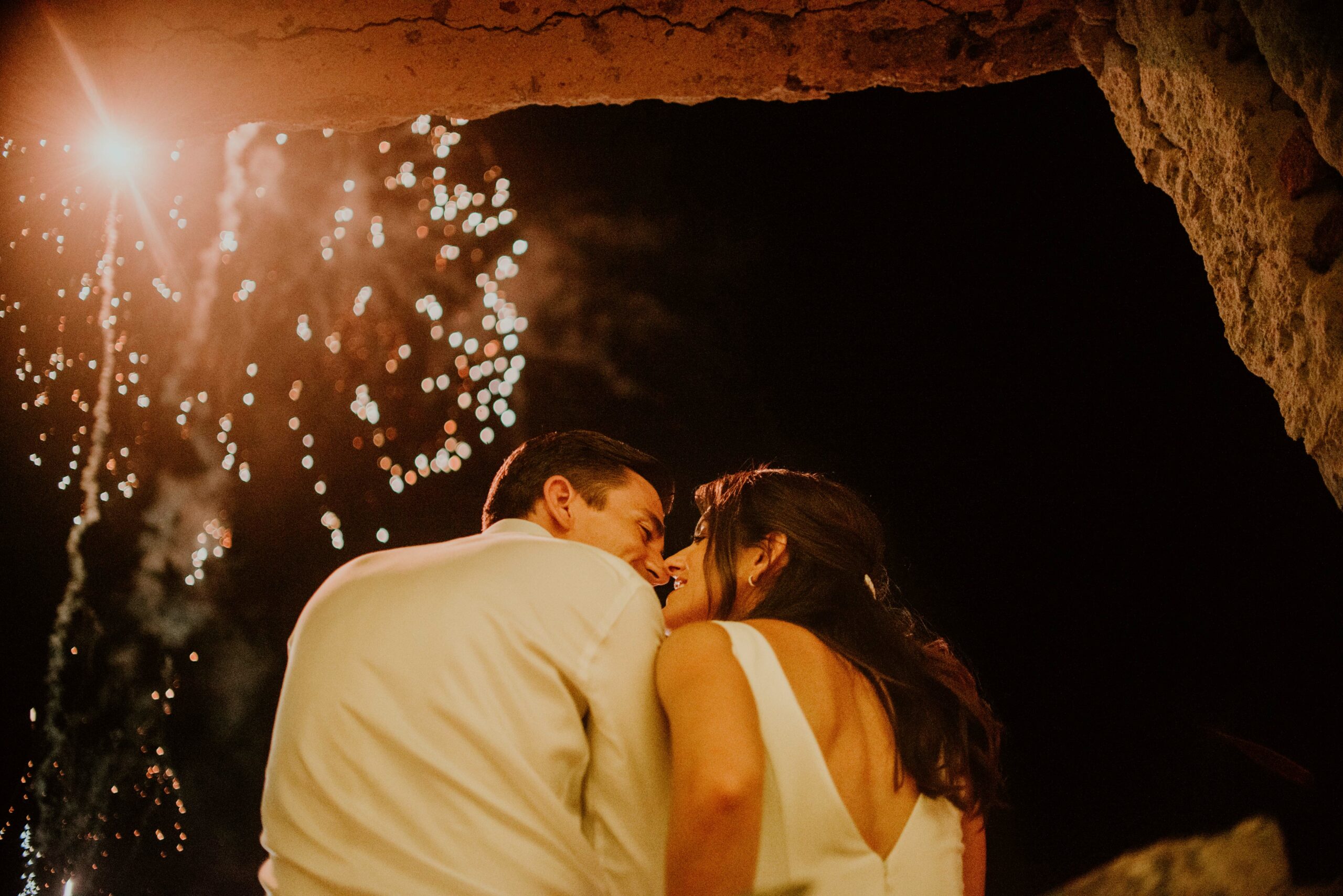 A couple kiss beneath a sky of fireworks