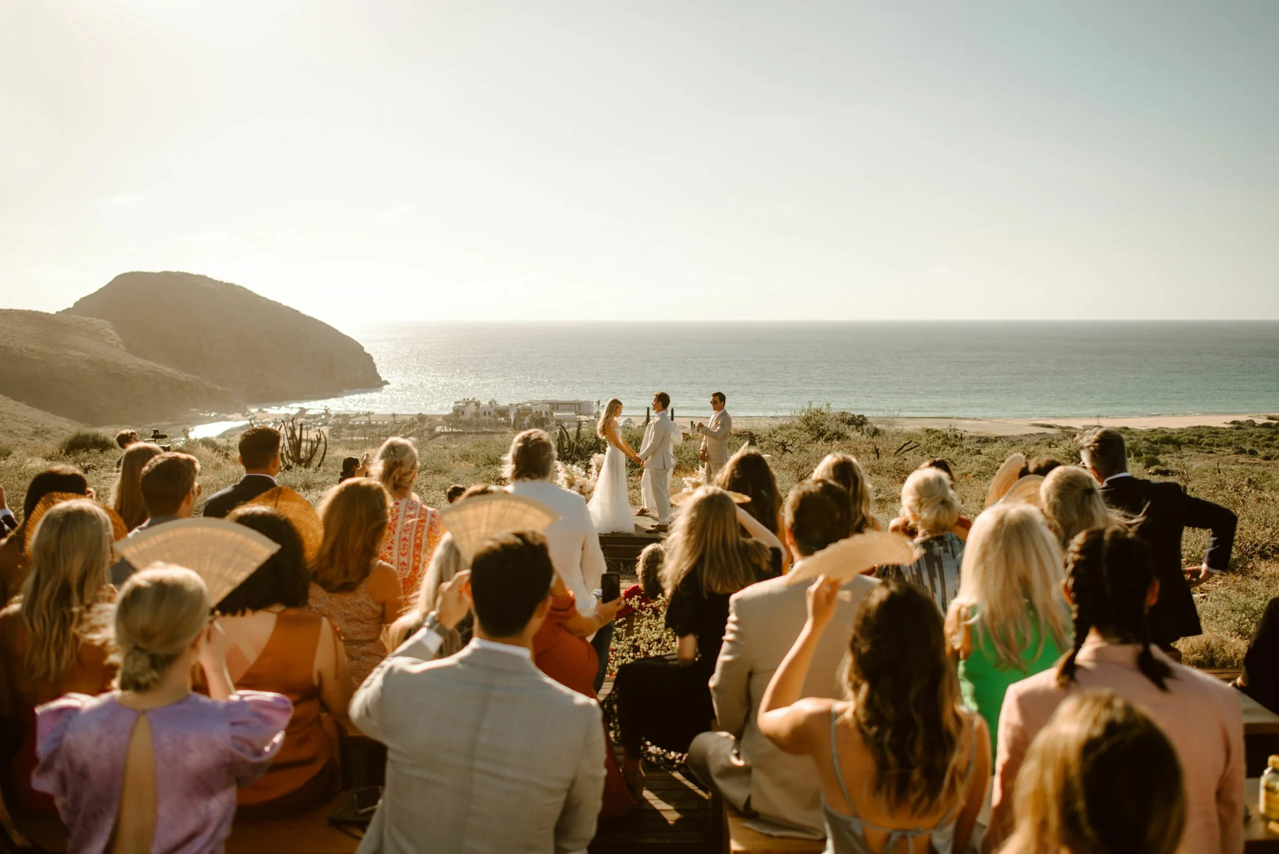 A crowd looks on towards a couple being wed by the ocean