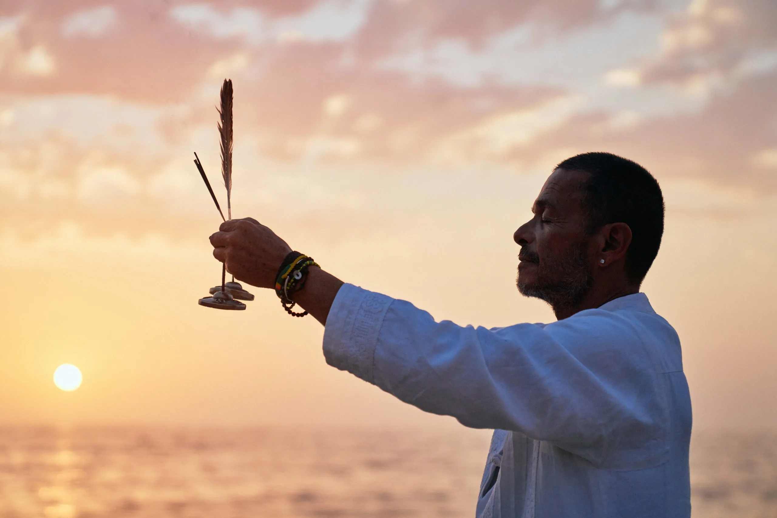 man holding incense in front of sunset