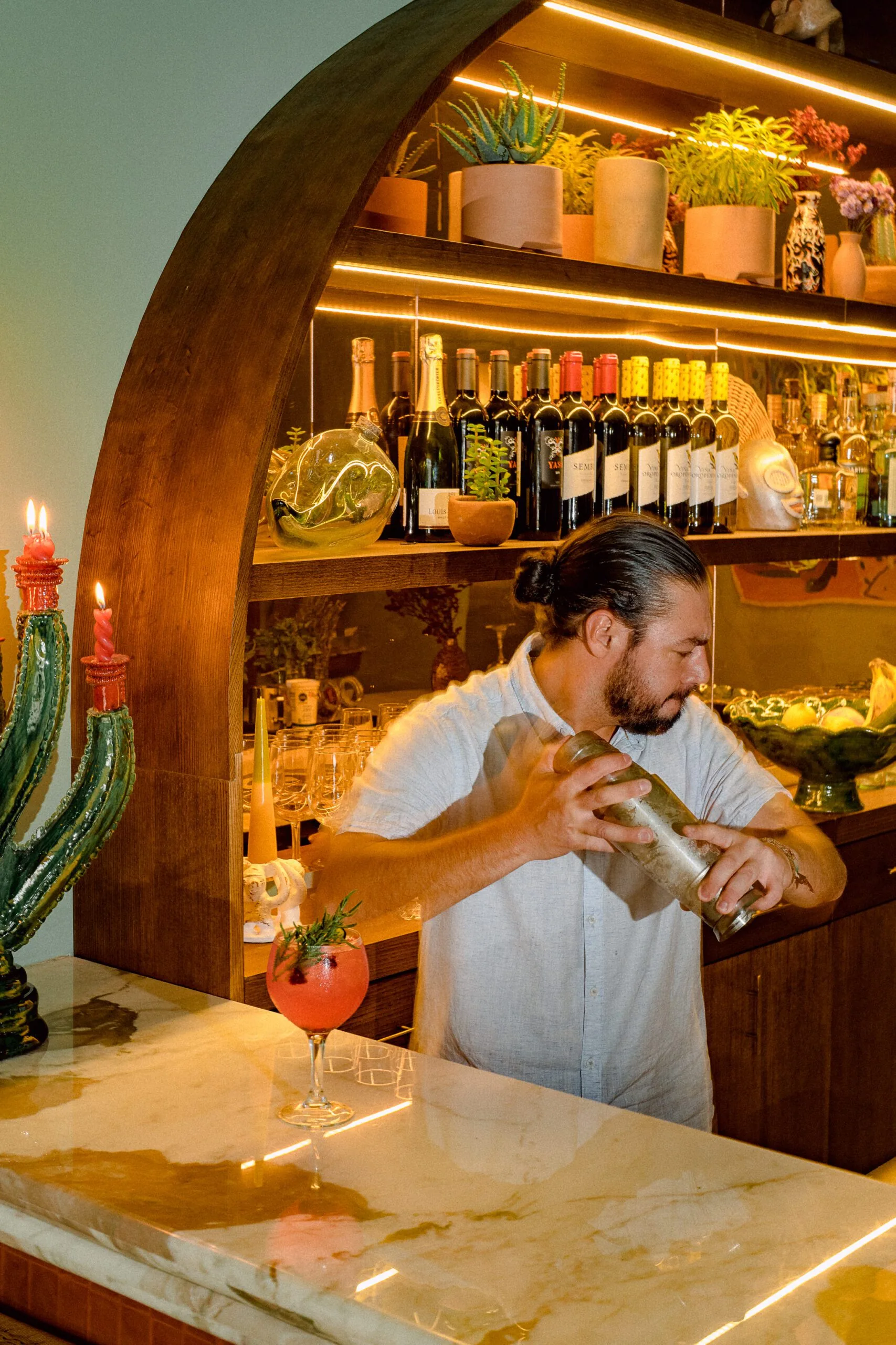 Man mixing a drink in front of a curved bar with cactus candleholder
