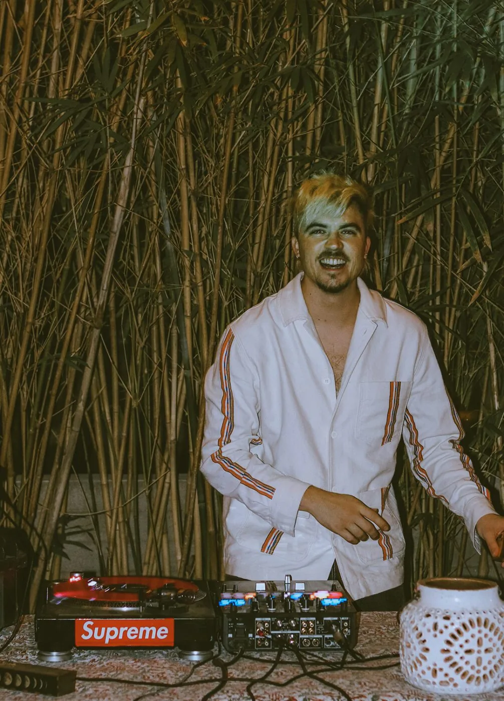 A DJ smiling for the camera in front of bamboo