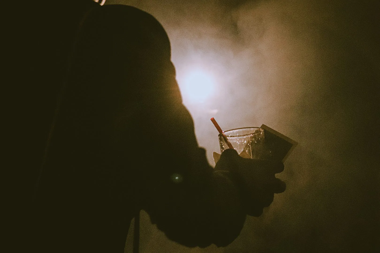 Artistic shot of a silhouette holding a glass amid smoke
