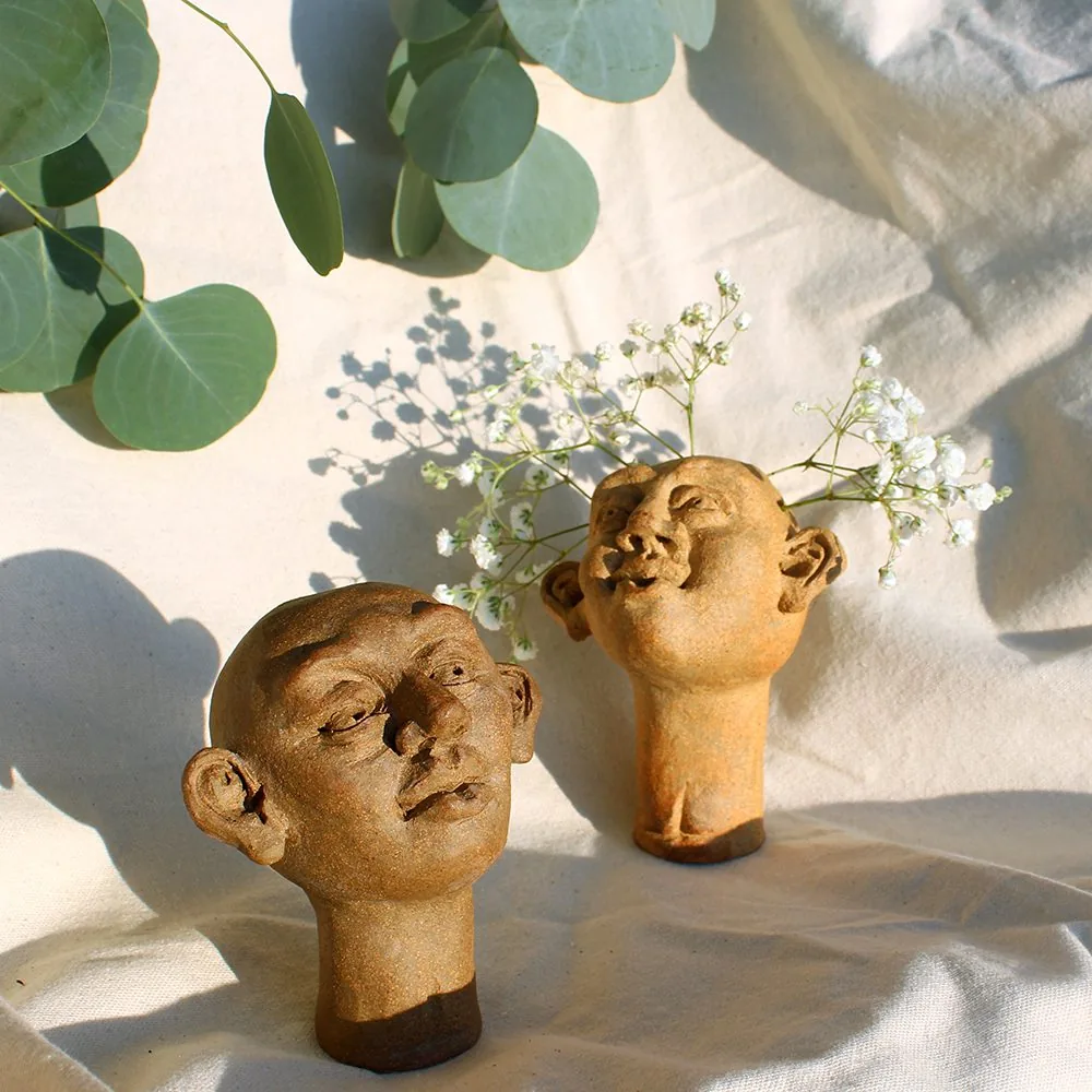 two head sculptures. one with flowers sticking out at the top