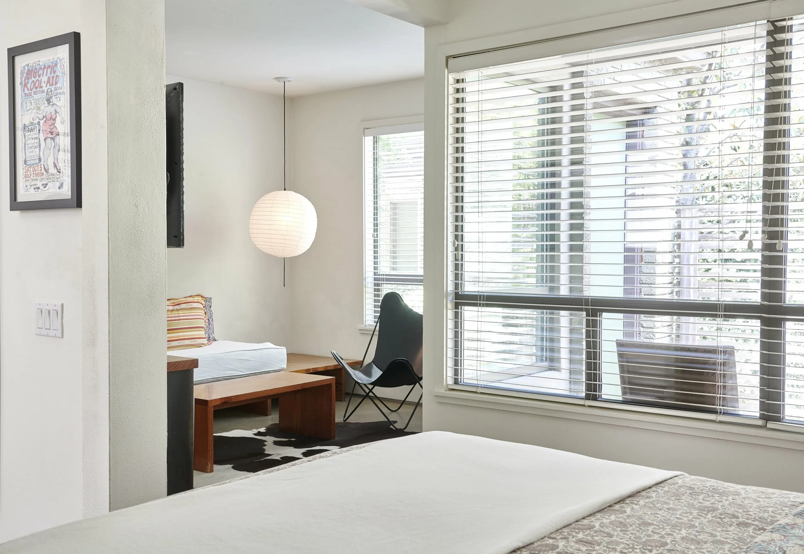 Interior of a room at Hotel San Jose, looking from the bed towards a built-in sofa, hanging paper lantern, and leather butterfly chair