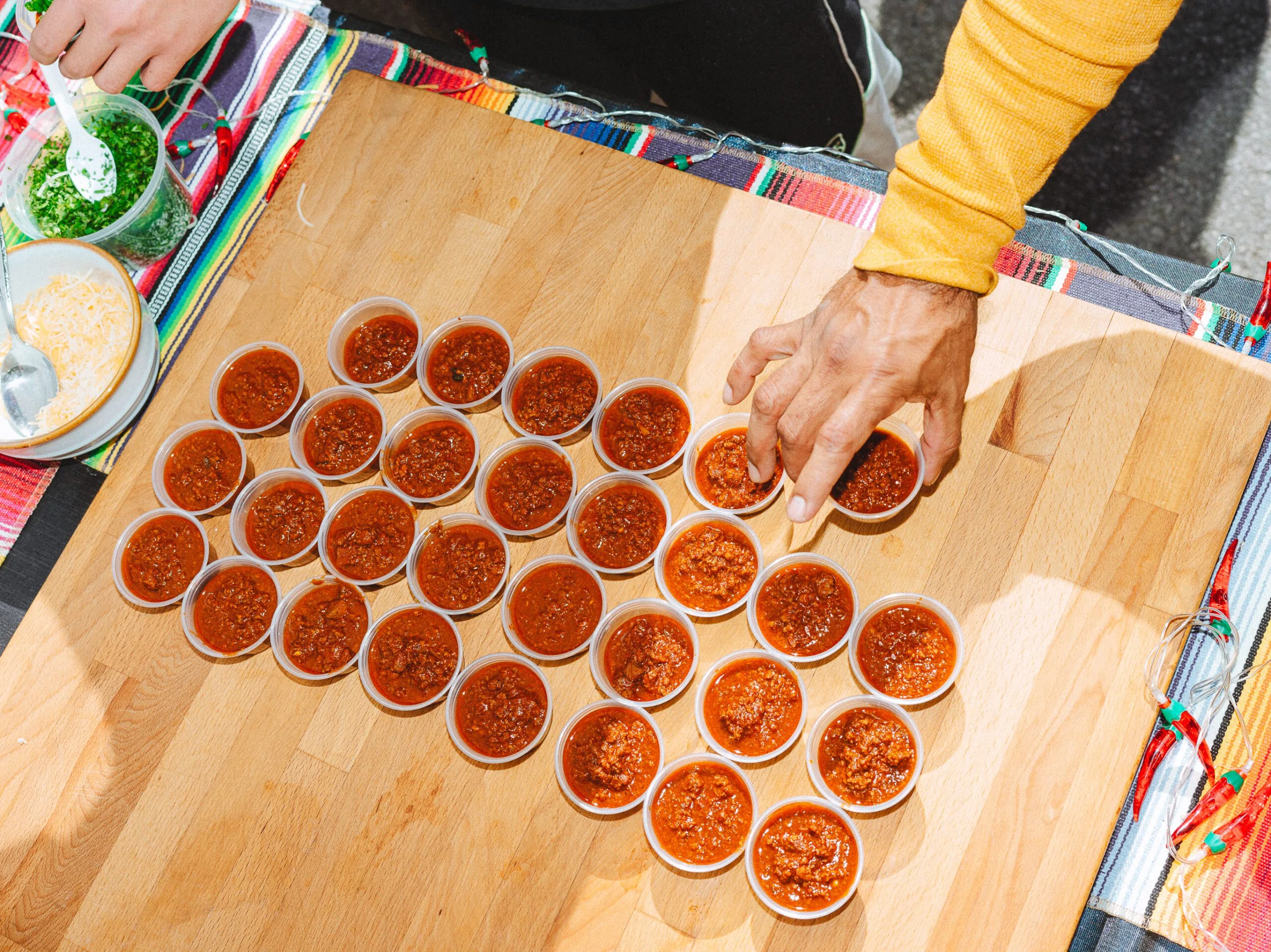 person reaching for a chili sample from a wooden board of samples
