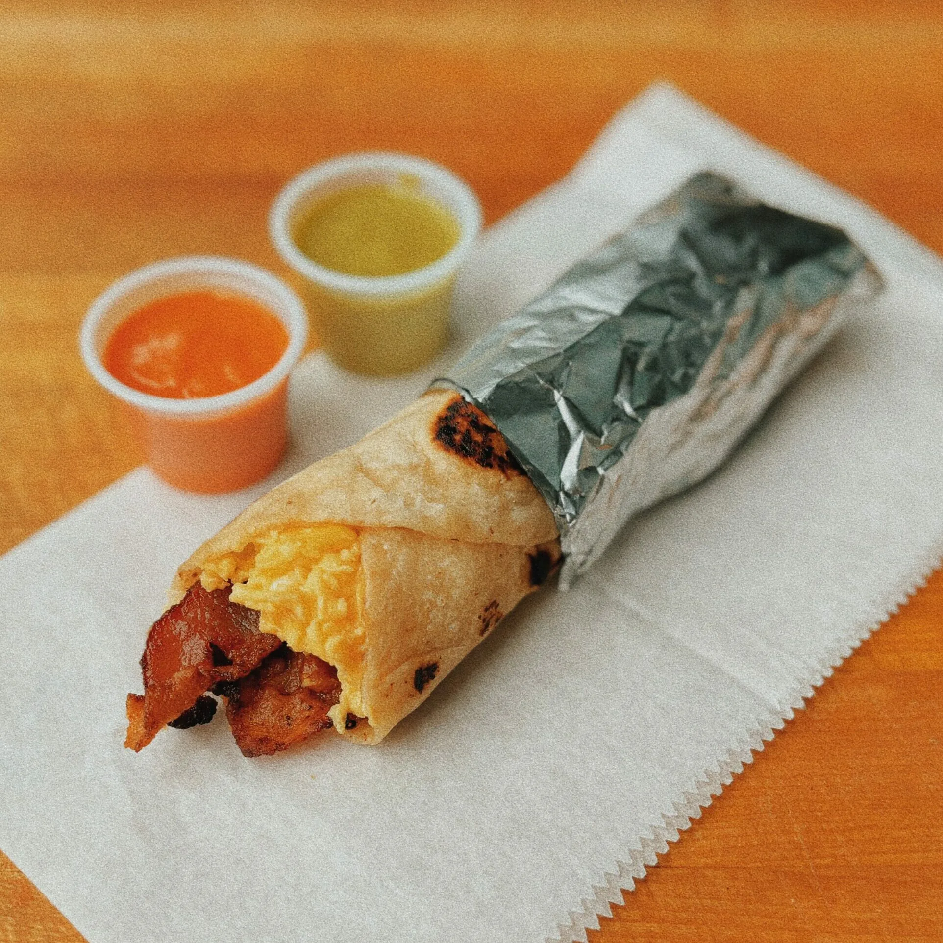 bacon egg burrito on a napkin beside two dipping sauces
