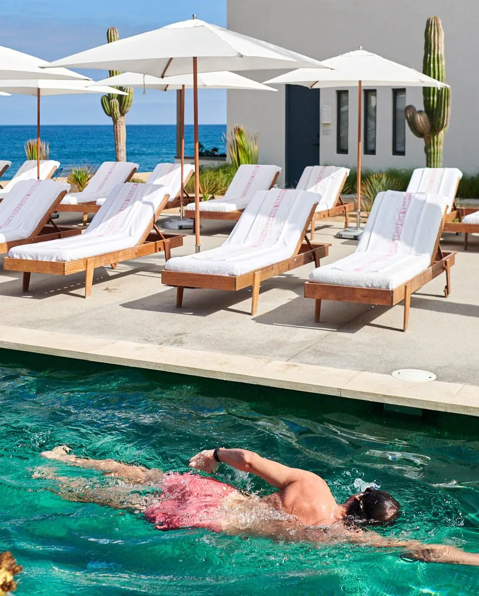 Man in shorts swimming in a pool in front of white beach chairs