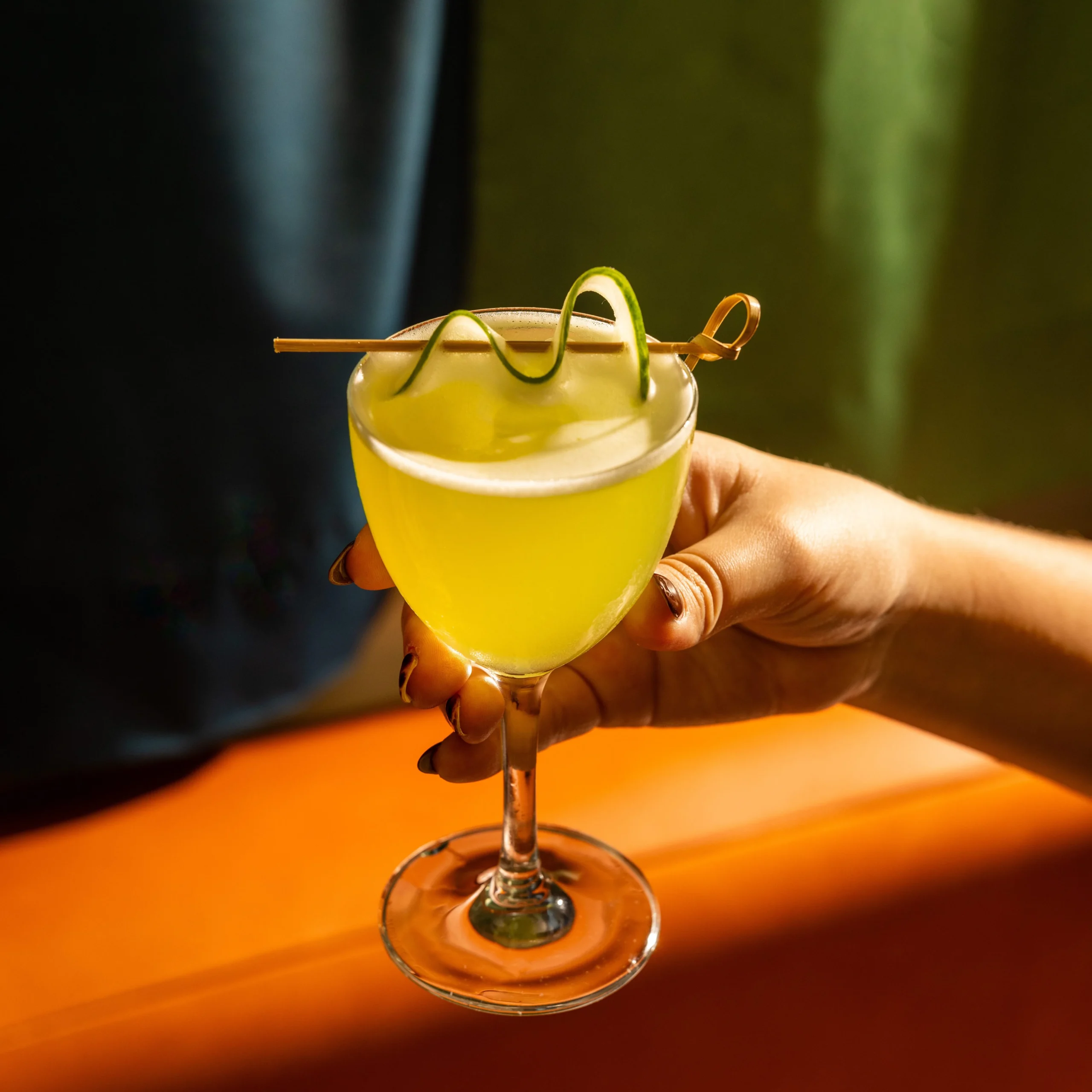 Hand holding a cocktail with a cucumber garnish