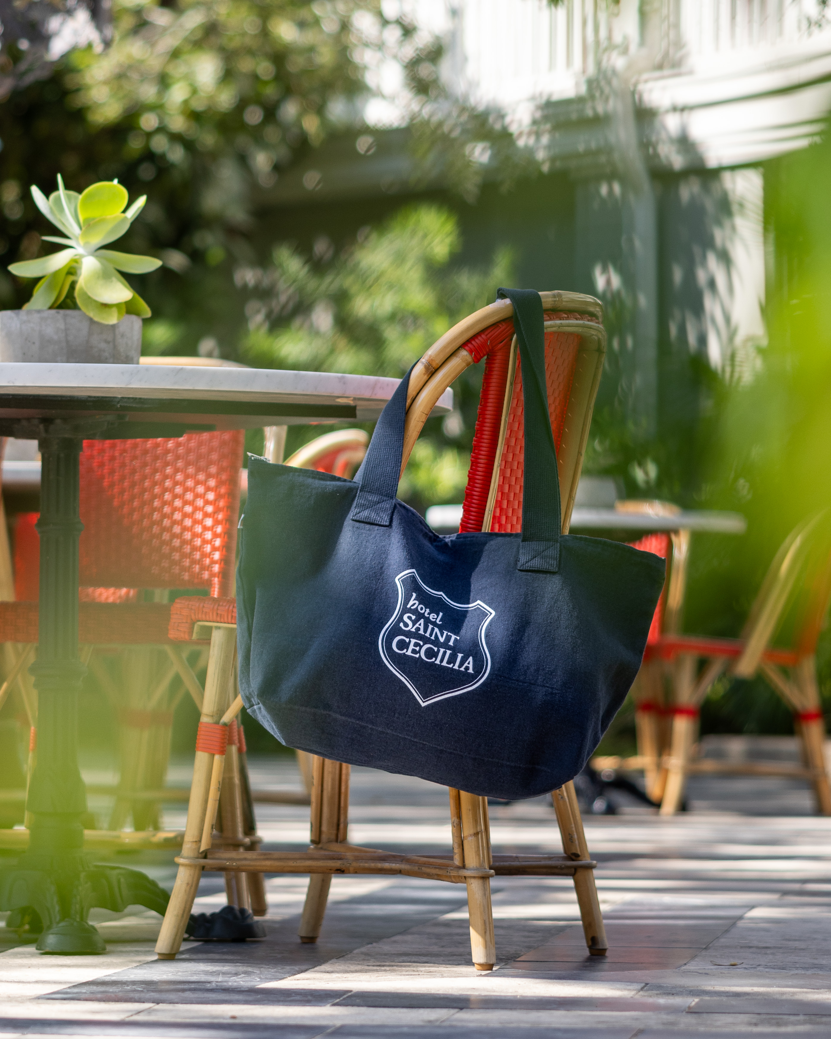 Hotel Saint Cecilia tote bag hanging off of a red chair in the courtyard